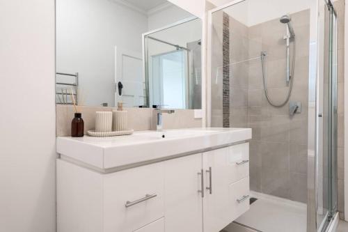 La salle de bains blanche est pourvue d'un lavabo et d'une douche. dans l'établissement 'The Zophey House' A Charming Coastal Cottage, à Rosebud