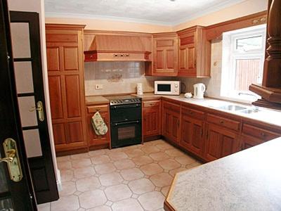 a kitchen with wooden cabinets and a black stove top oven at Tyn Y Graig Cottage in Crynant