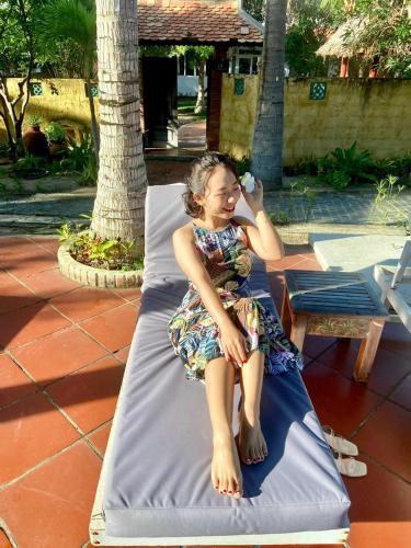 a girl in a dress sitting on a bed at Full Moon Village Resort in Mui Ne