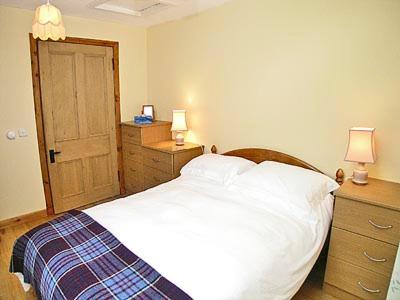 1 dormitorio con cama blanca y puerta de madera en Milton Byre, en Rothesay