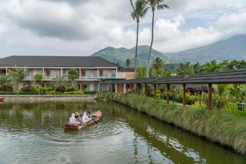 people in a canoe on a river in front of a building at Villa Rancabango Hotel & Resort Garut in Tarogong