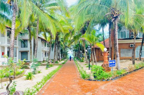a walkway lined with palm trees in front of a building at Kega Lighthouse Resort Bình Thuận in Ke Ga