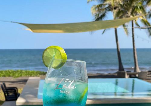a glass of liquid with a lime in front of the ocean at Lali Beach Hotel Boutique in Sonsonate