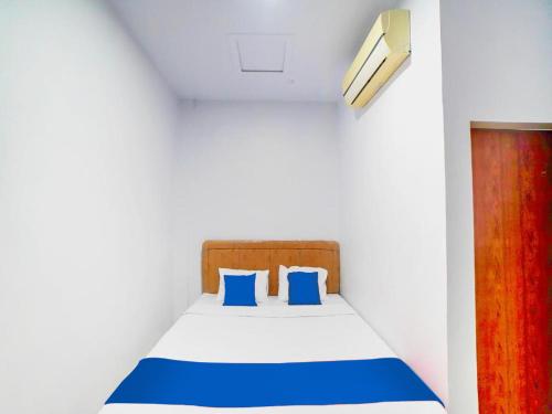 uma cama com almofadas azuis num quarto branco em Sg Premium Guest House By Helocus em Medan