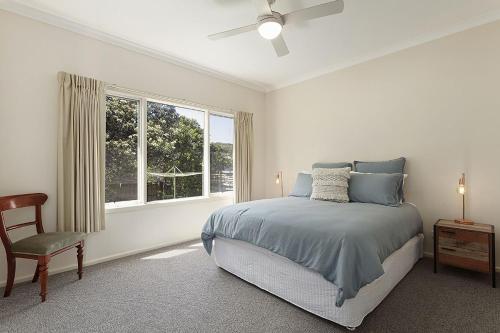 a bedroom with a bed and a chair and a window at Curragundi in Point Lonsdale