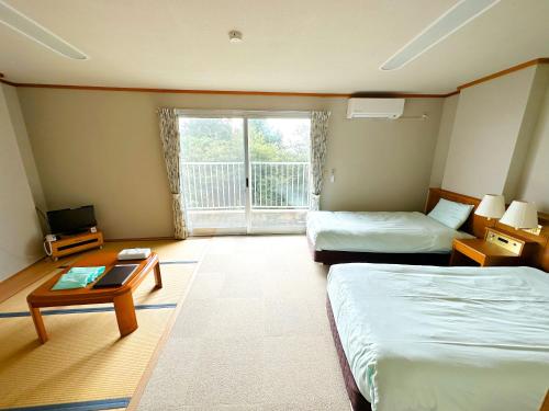 a room with two beds and a table and a window at 森林公園スイス村 風のがっこう京都 in Kyotango