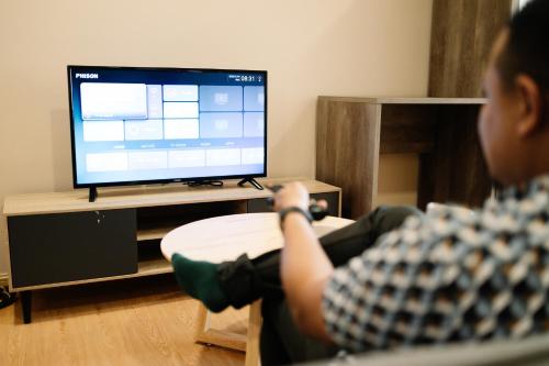 a man sitting on a chair in front of a television at Mahkota Valley Suite by Timorra in Kuantan