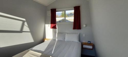 a bedroom with a bed with red curtains and a window at Omarama TOP10 Holiday Park in Omarama