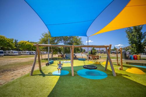 a child standing on a swing set in a playground at Omarama TOP10 Holiday Park in Omarama