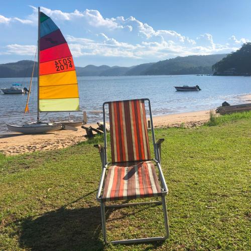 a chair sitting on the grass next to a sail boat at Deerubbin Boat House in Dangar Island