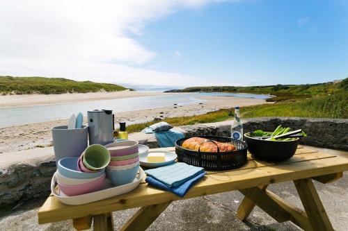 a picnic table with plates and dishes on the beach at Ty Glan Y Mor in Aberffraw