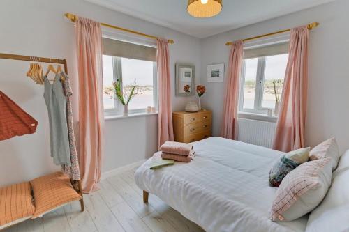 a bedroom with a bed and two windows with pink curtains at Ty Glan Y Mor in Aberffraw
