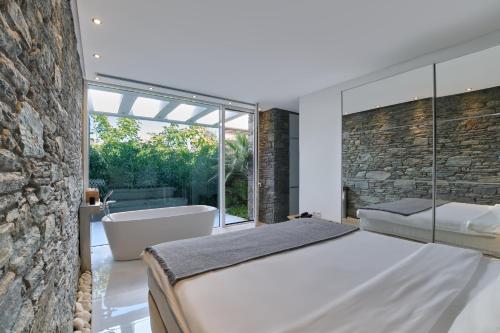 a bedroom with a large bed and a bath tub and a stone wall at A - Luxury Villas in Plomarion