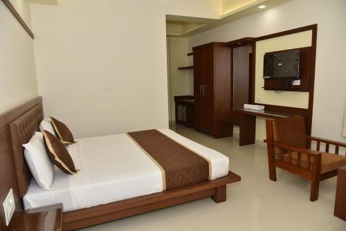 a bedroom with a bed and a chair and a television at Hotel Adithya View in Dharmastala