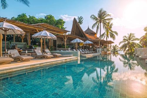 einen Pool in einem Resort mit Stühlen und Sonnenschirmen in der Unterkunft Bali Mandira Beach Resort & Spa in Legian