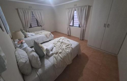 a white bedroom with two beds and two windows at M&M Self Catering in Richards Bay