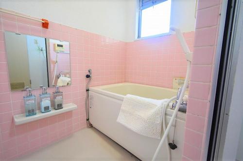Baño de color rosa con bañera y lavamanos en coco de minpaku en Sumiyoshi