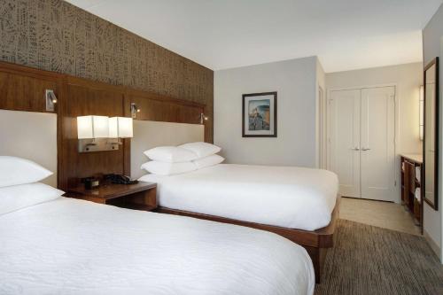 a hotel room with two beds with white sheets at Embassy Suites by Hilton Detroit Metro Airport in Romulus