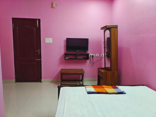 um quarto com paredes cor-de-rosa, uma cama e uma televisão. em Le Paradise Inn em Pondicherry