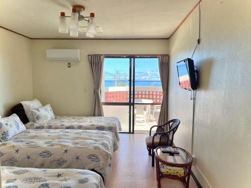 a hotel room with two beds and a television at ビーチサイドペンションみーばる in Nanjo