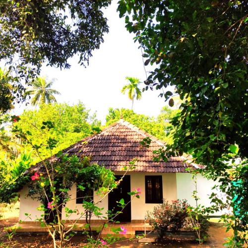 a small white house with a thatched roof at Munroe Inn Homestay in Kollam