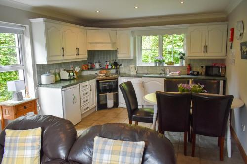 ダングローにあるSimply Donegal Adrihidbeg Cottageの白いキャビネット、テーブルと椅子付きのキッチンが備わります。