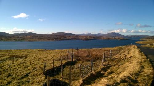a fence in a field next to a body of water at Harsgeir View Holiday Cottage -Wifi Go green in Breaclete