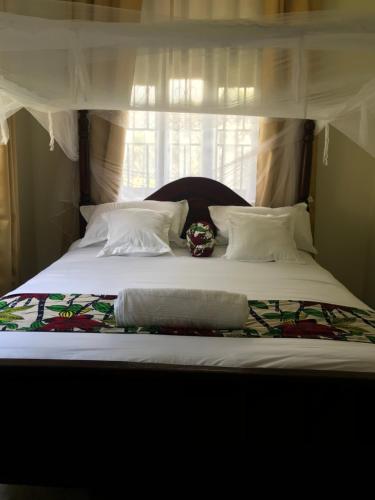 a large bed with white sheets and a window at The Fortuna Apartment in Kabale