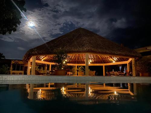 a building with a thatched roof next to a pool at night at Hotel Santo Vanuatu in Luganville