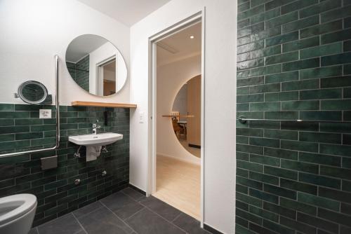 uma casa de banho com azulejos verdes do metro e um lavatório em Tailormade Hotel BAB Bachenbülach em Bachenbülach