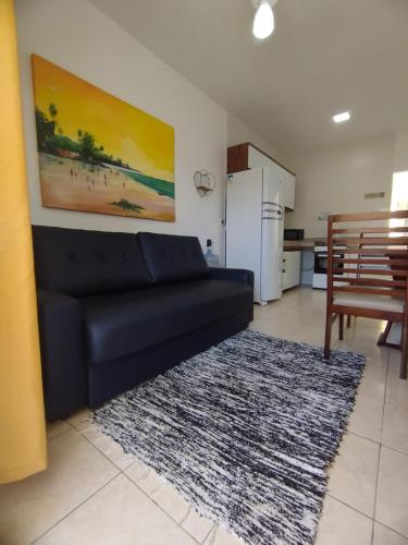 ein Wohnzimmer mit einem schwarzen Sofa und einer Küche in der Unterkunft Sweet Room Coroa Vermelha in Santa Cruz Cabrália