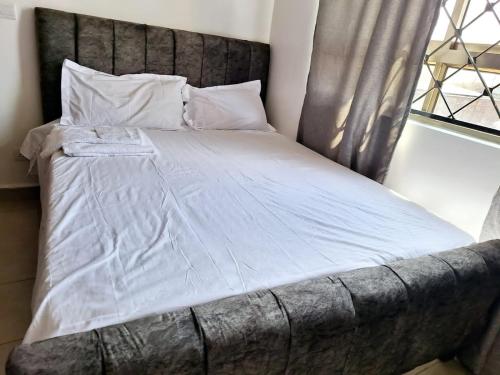 uma cama com lençóis brancos e almofadas ao lado de uma janela em Jkia 3 bedroom greatwall gardens phase 4 em Athi River
