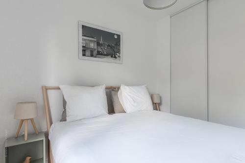 - un lit blanc avec des oreillers blancs et une photo sur le mur dans l'établissement Chez André By Plaza - Proche Disneyland Paris, à Magny-le-Hongre