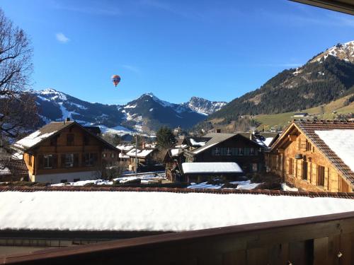 a town in the mountains with a hot air balloon in the sky at Wonderful apartment overlooking the Swiss alps in Chateau-d'Oex
