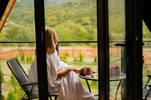 a little girl sitting at a table with a cup of coffee at Oda Riverside Cottages in Aragvispiri