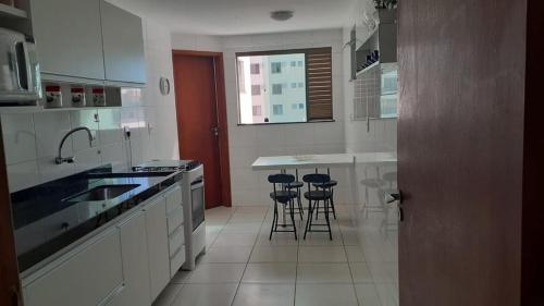 a kitchen with white cabinets and bar stools at Férias em Família Apartamento Temporada in Cabo Frio