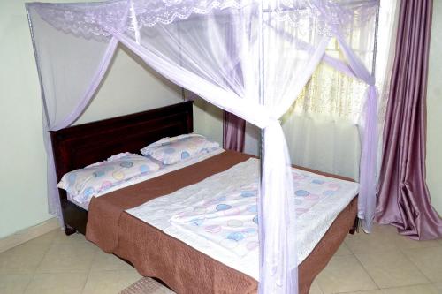 een slaapkamer met een hemelbed en paarse gordijnen bij olive Palm Suites in Njeru