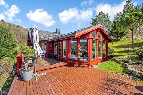 a red house with a deck and an umbrella at Gemütliches helles Ferienhaus am See mit Panoramaseeblick + Hütte und nahe Meer in Lyngdal