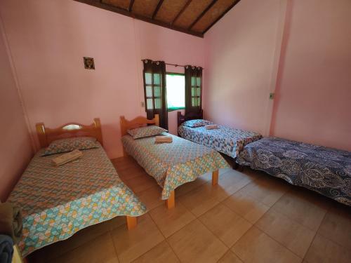 três camas num quarto com paredes cor-de-rosa em Govinda Moeda Pousada em Moeda