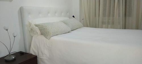 a white bed with white sheets and pillows on it at Habitaciones individuales en apartamento turístico in Madrid