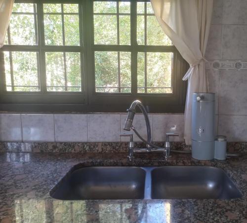 a sink in a kitchen with two windows at La Casita del Río in Villa Ciudad Parque