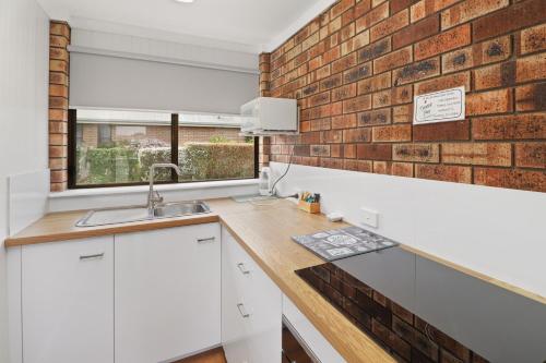 a kitchen with white cabinets and a brick wall at Kellraine Holiday Units in St Helens