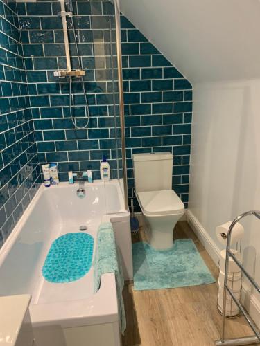 een badkamer met een bad, een toilet en blauwe tegels bij Queens Cottage Salisbury in Salisbury