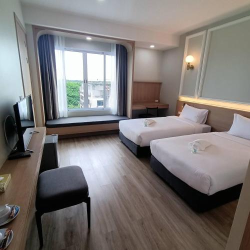 a hotel room with two beds and a window at Mayflower Grande Suite Hotel in Phitsanulok