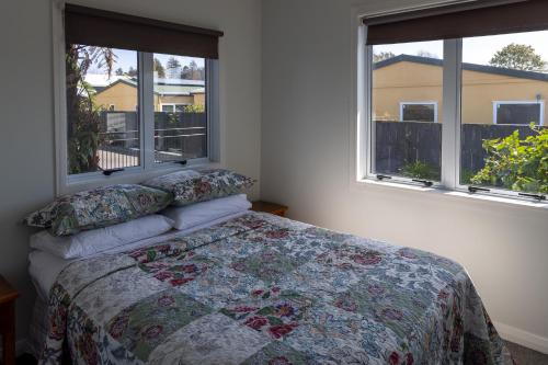 a bedroom with a bed and two windows at Tui nest in Whangamata
