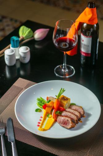 a plate of food on a table with a glass of wine at La Charm Hoi An Hotel & Spa in Hoi An