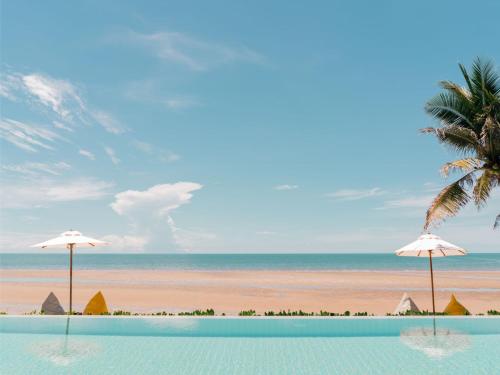 a swimming pool with two umbrellas and the beach at RELO' The Urban Escape - Huahin in Cha Am