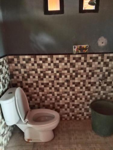 a bathroom with a toilet and a tiled wall at Lestari Cottages in Kododa
