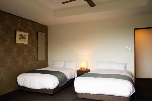 duas camas num quarto de hotel com lençóis brancos em ホテルコンドミニアム土花土花 em Onna