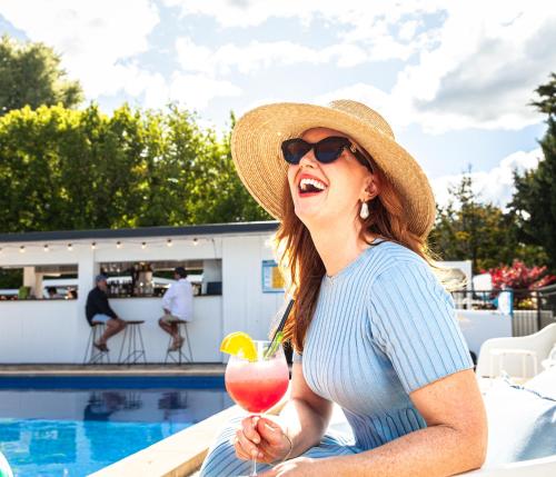 una mujer sentada junto a una piscina con una bebida en The Oriana Orange - Retro Hotel & Resort en Orange